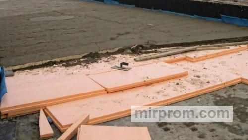 Мастер укладывает плиты оранжевого утеплителя на песчаную подушку