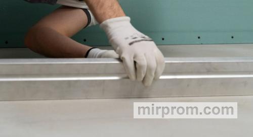 Процесс проверки ровности бетонной стяжки металлическим правилом перед началом укладки