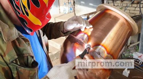 Сварщик в защитной маске варит медную пластину в среде аргона